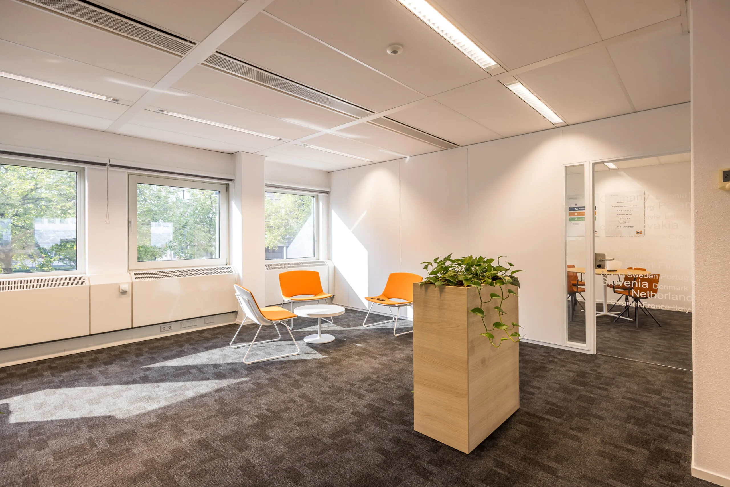Moderne wachtruimte aan de Varrolaan met oranje stoelen, veel lichtinval en een glazen deur naar een vergaderruimte.