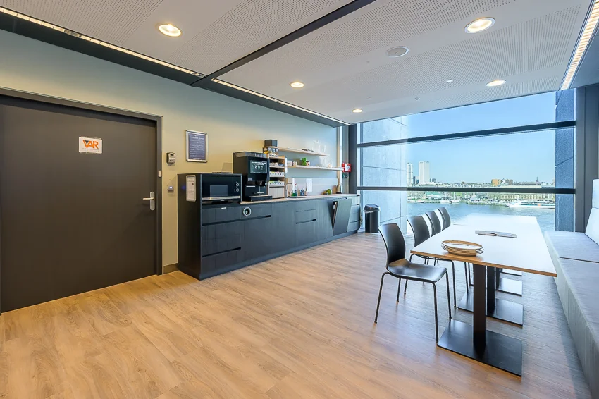 Moderne pantry met koffieautomaat en zitgedeelte aan de Wilhelminakade met uitzicht op de skyline van Rotterdam.