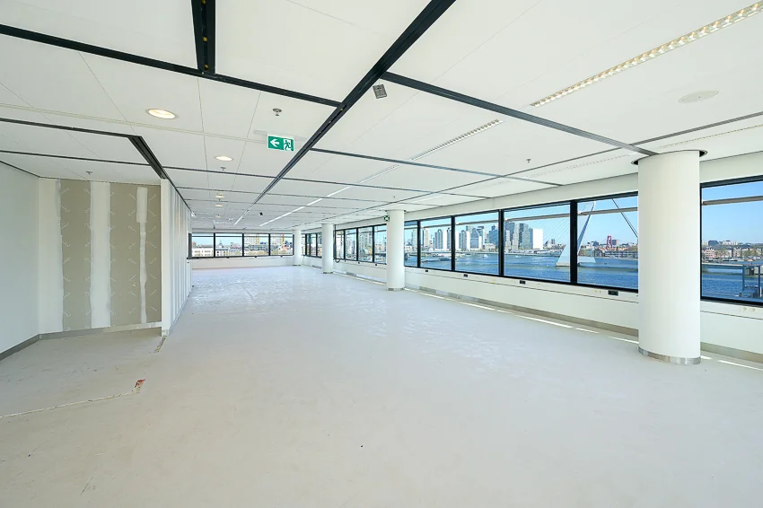 Licht en modern leeg kantoorpand aan de Wilhelminakade met uitzicht op de skyline van Rotterdam en de Erasmusbrug.