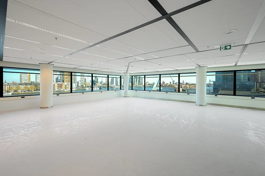 Lichte, lege kantoorruimte met grote ramen en uitzicht op de skyline aan de Wilhelminakade in Rotterdam.