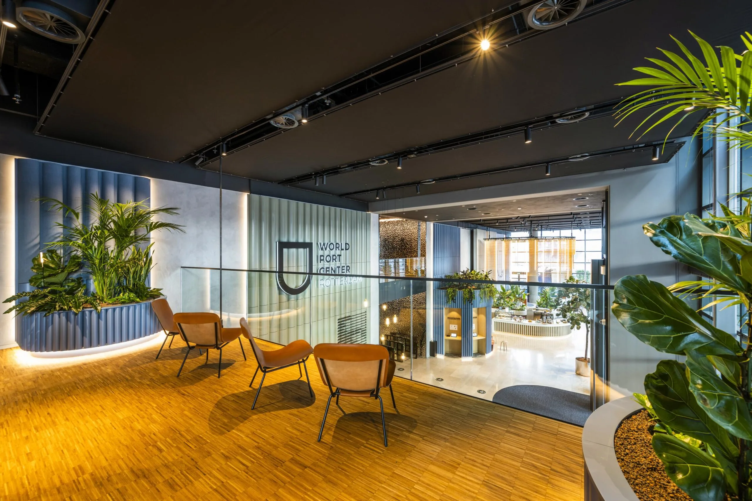Moderne, lichte ontvangsthal van het World Port Center Rotterdam met houten vloer, veel groen en loungezitjes.