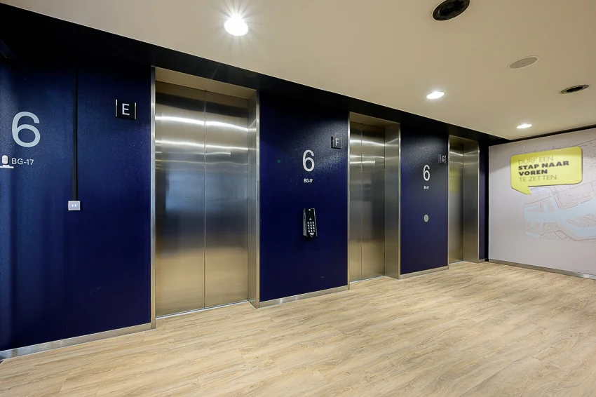 Liftlobby op de zesde verdieping van een modern gebouw aan de Wilhelminakade, met drie liften en houten vloer.