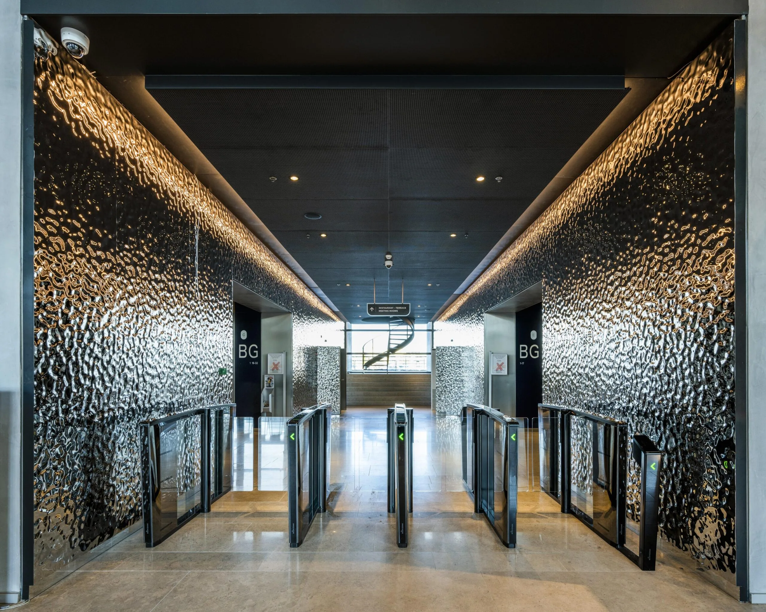 Moderne entreehal met toegangspoortjes en glanzende, golvende wandpanelen aan de Wilhelminakade.