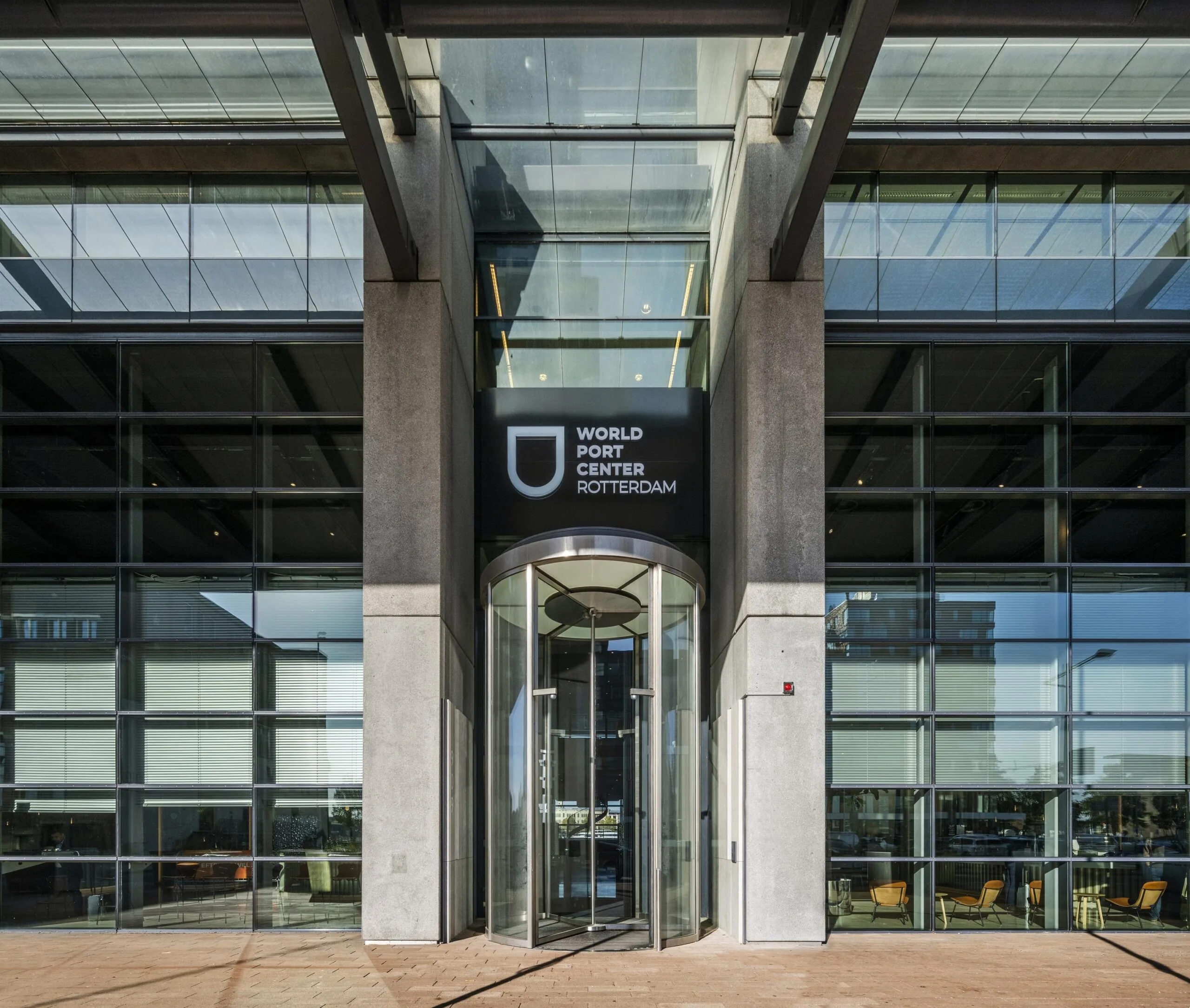 Ingang van het World Port Center aan de Wilhelminakade in Rotterdam met een glazen draaideur en modern gevelontwerp.