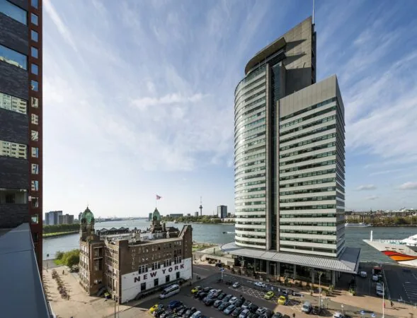 Uitzicht op de Wilhelminakade in Rotterdam met Hotel New York en het moderne kantoorgebouw De Rotterdam aan de rivier.