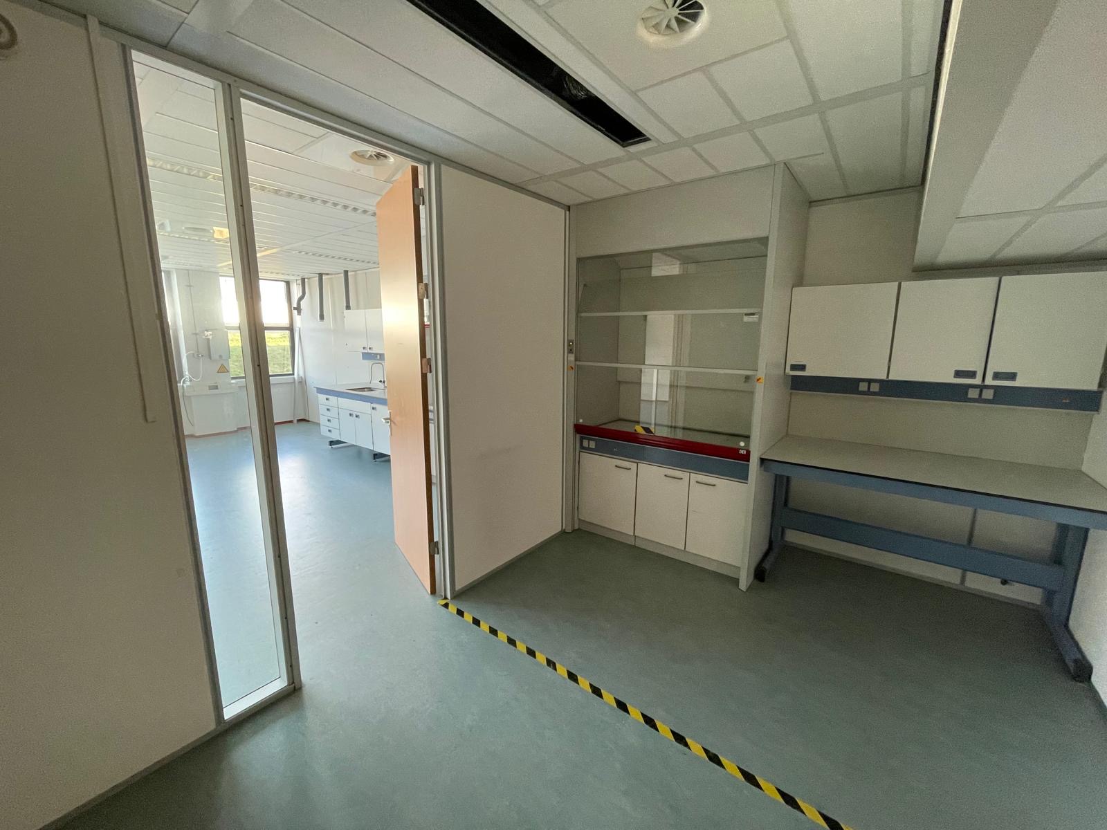 Leeg laboratorium met werktafels, opbergkasten en een open schuifdeur aan de Laan van S-Gravenmade.