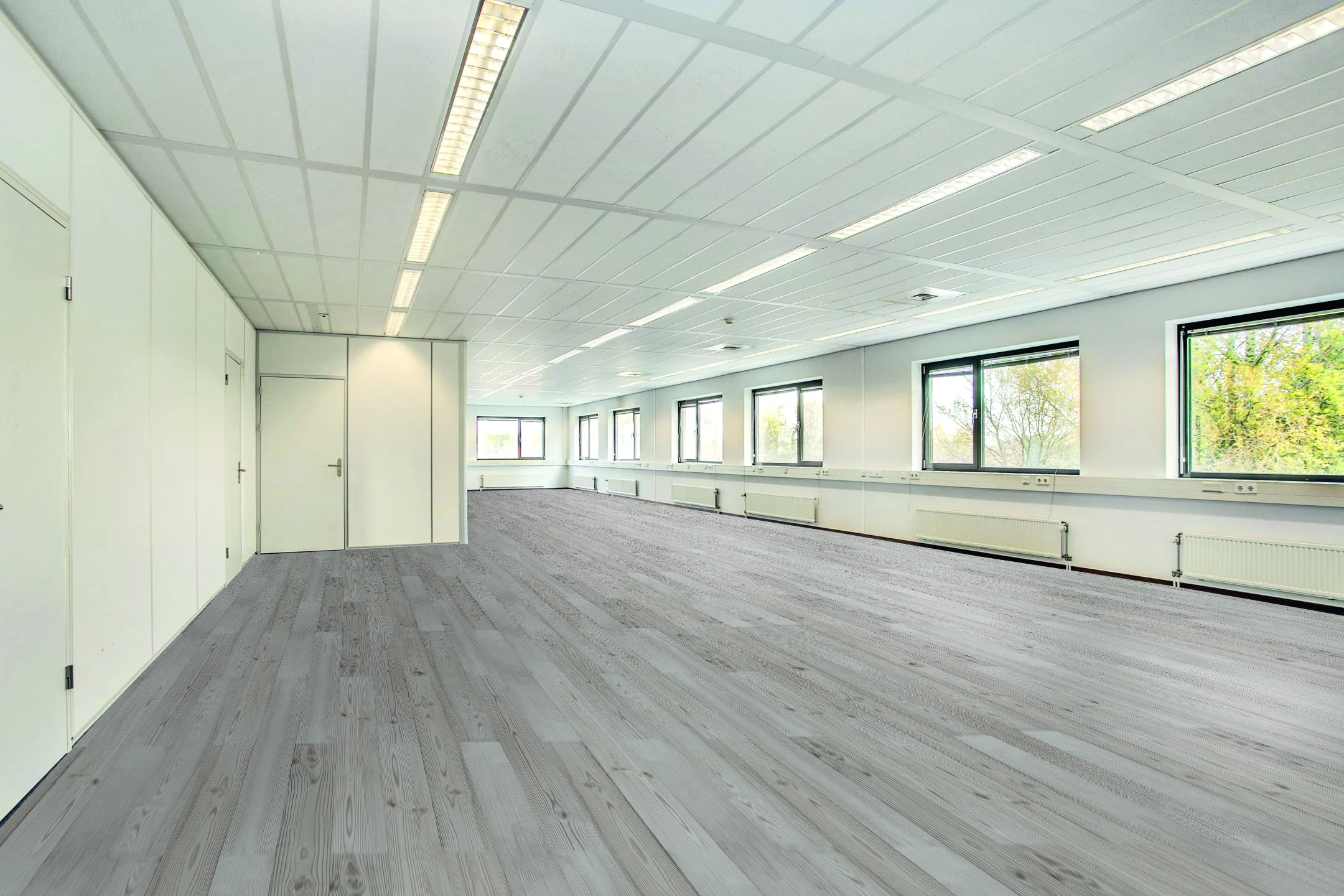 Lichte, lege kantoorruimte aan de Laan van S-Gravenmade met grote ramen en grijs houten vloer.