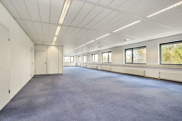 Lichte, lege kantoorruimte aan de Laan van S-Gravenmade met blauwe vloerbedekking en grote ramen.