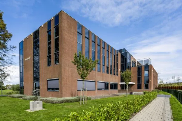 Modern roodbrick kantoorgebouw aan de Oranjebaan met grote ramen en een goed onderhouden groene buitenruimte.