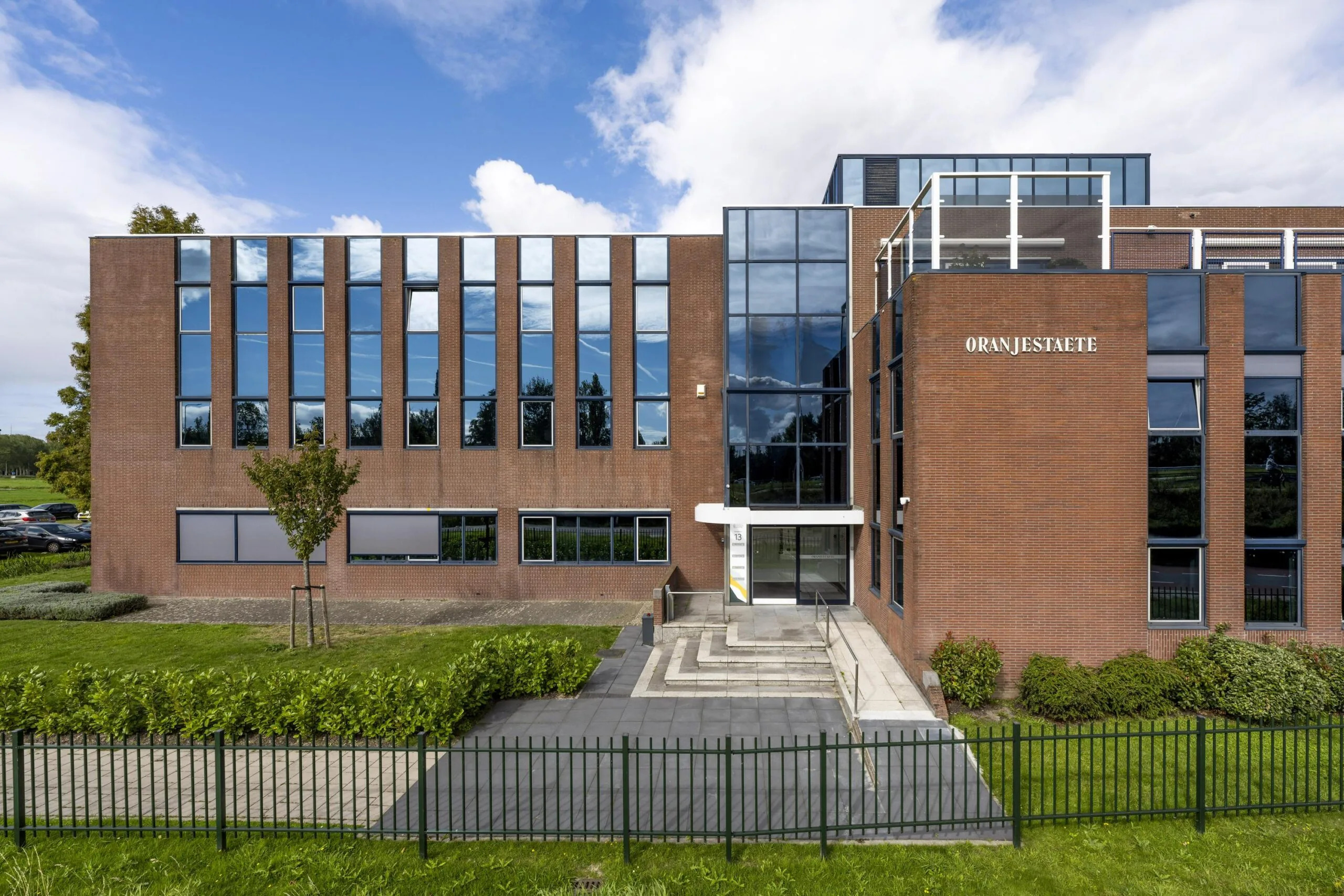 Vooraanzicht van het kantoorgebouw Oranjestaete aan de Oranjebaan met rode bakstenen gevel en grote raampartijen.