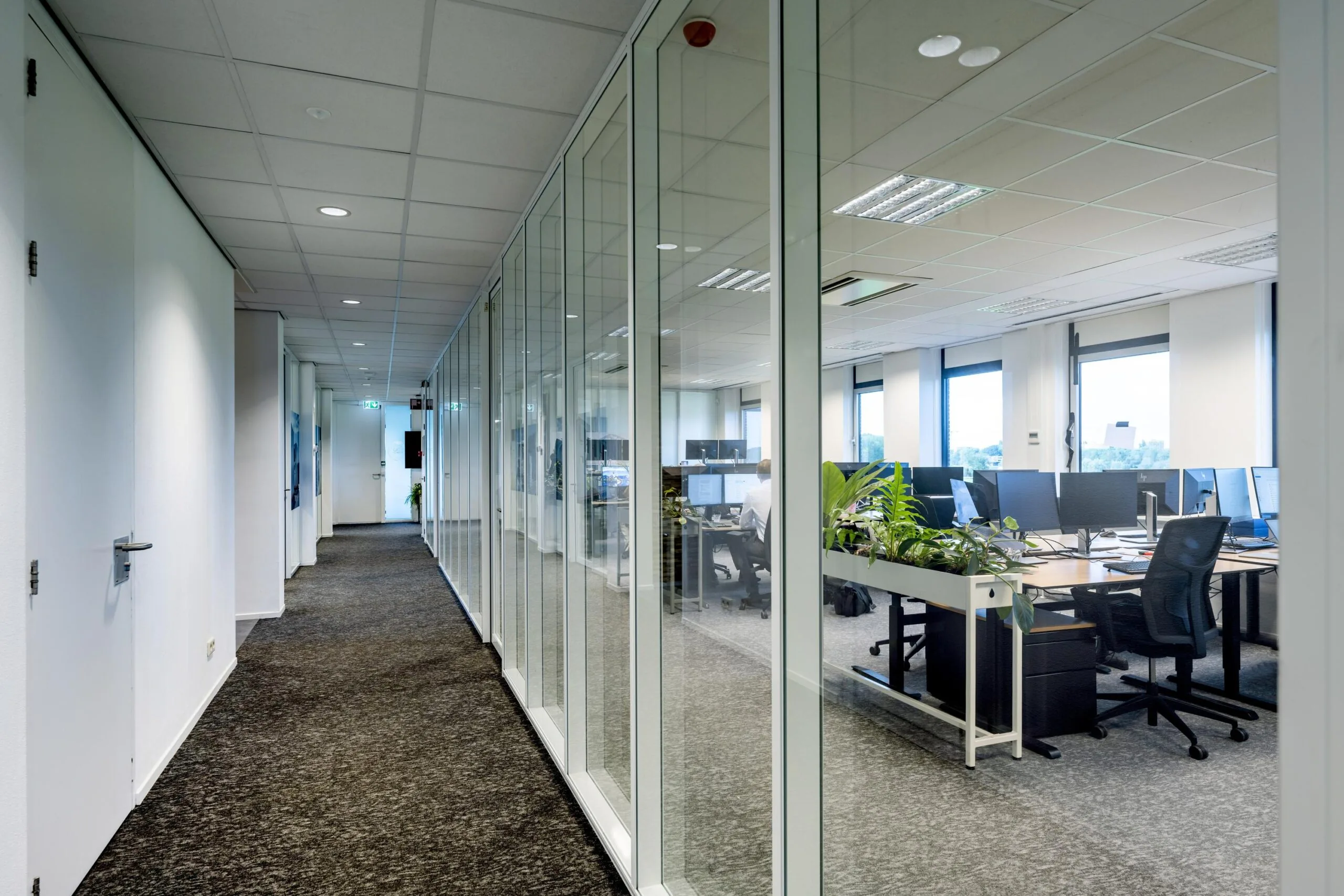 Moderne kantoorgang met glazen wanden en zicht op een open kantoorruimte aan de Oranjebaan.