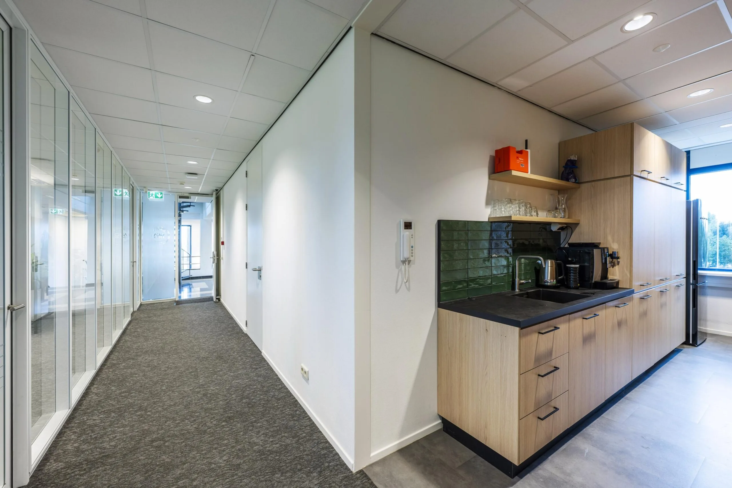 Moderne kantoorruimte aan de Oranjebaan met een gang en een pantry voorzien van houten keukenkasten en een koffiezetapparaat.