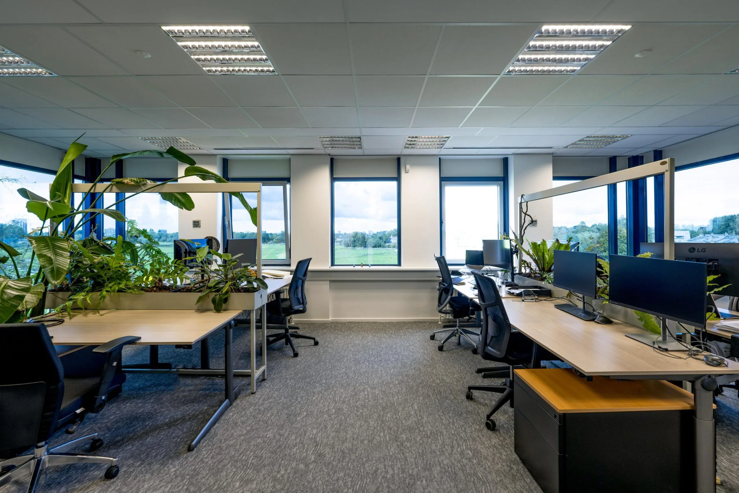 Modern kantoorinterieur aan de Oranjebaan met werkplekken, bureaustoelen, computers en veel groene planten.
