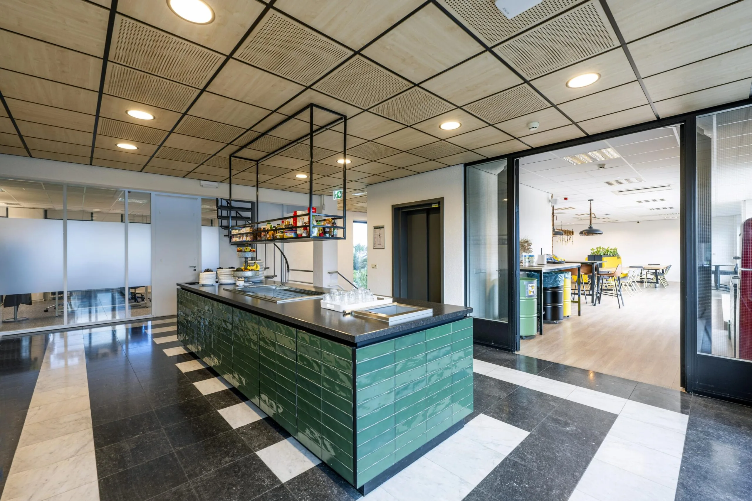 Moderne bedrijfskeuken en kantine aan de Oranjebaan met groene tegelafwerking en open zitruimte.