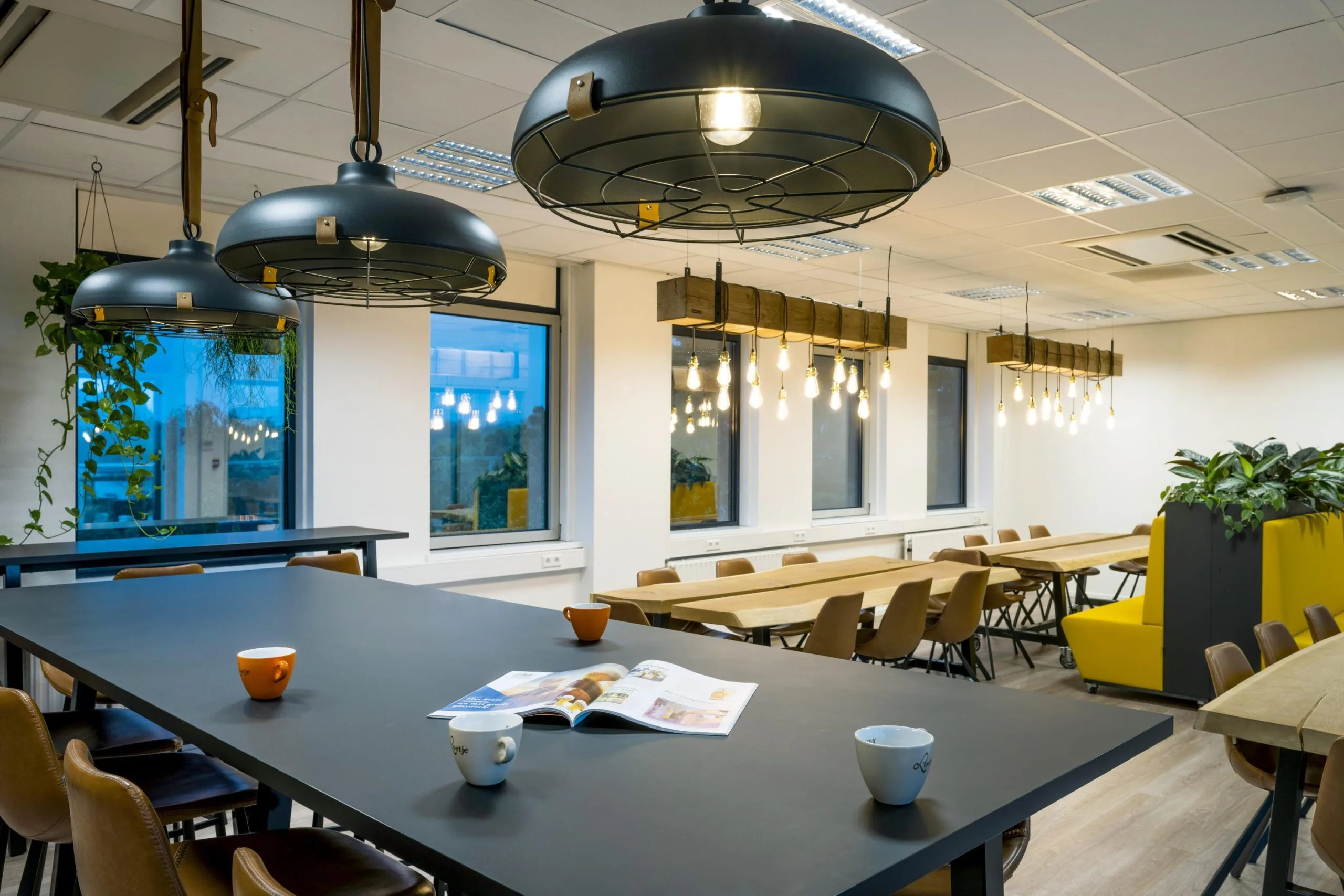 Moderne, sfeervol verlichte kantoorruimte met lange houten tafels, hanglampen en planten.