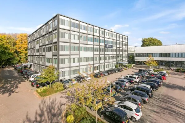 Kantoorgebouw aan de Hoefsmidstraat met parkeerterrein vol auto's op een zonnige dag.