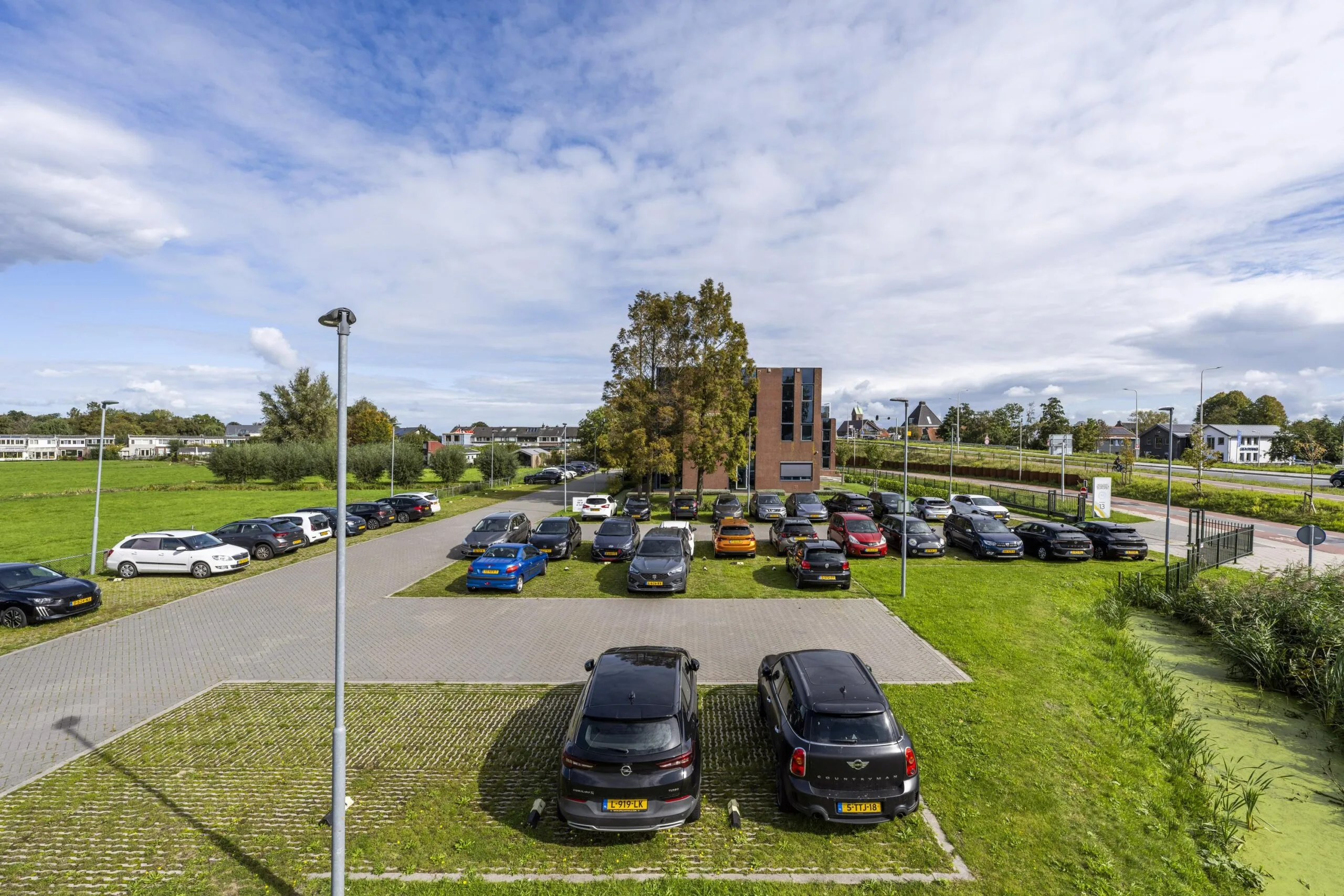 Parkeerterrein bij een modern kantoorgebouw aan de Oranjebaan, omgeven door groen en woonwijken.