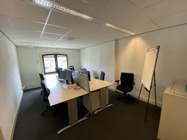 Kleine kantoorruimte aan de Burgemeester van Karnebeeklaan met meerdere bureaus, bureaustoelen, computerschermen en een flip-over.