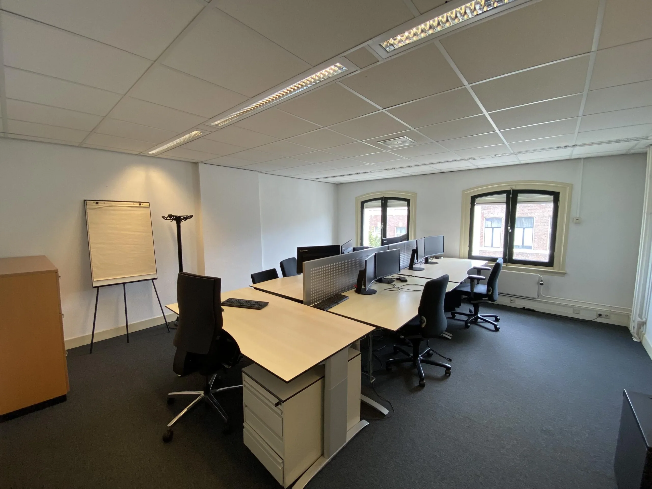 Moderne kantoorruimte aan de Burgemeester van Karnebeeklaan met meerdere werkplekken, bureaustoelen, computers en een flip-over.