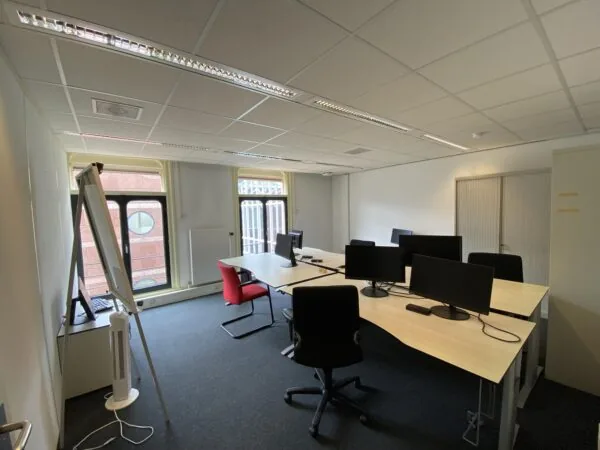 Kantoorruimte aan de Burgemeester van Karnebeeklaan met bureaus, computers, stoelen en een flip-over bij het raam.