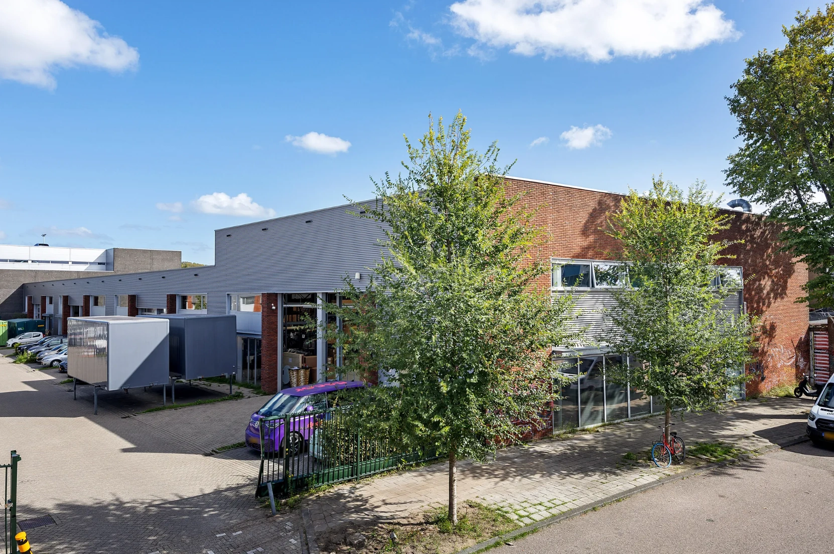Bedrijfsgebouw aan de Schaafstraat met parkeerplaatsen, bomen en een paar geparkeerde voertuigen op een zonnige dag.