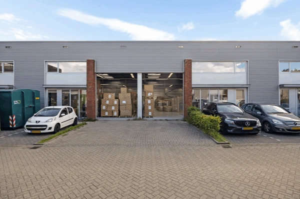 Bedrijfsgebouw aan de Schaafstraat met openstaande loodsdeuren en dozen op pallets binnen, omringd door geparkeerde auto's.