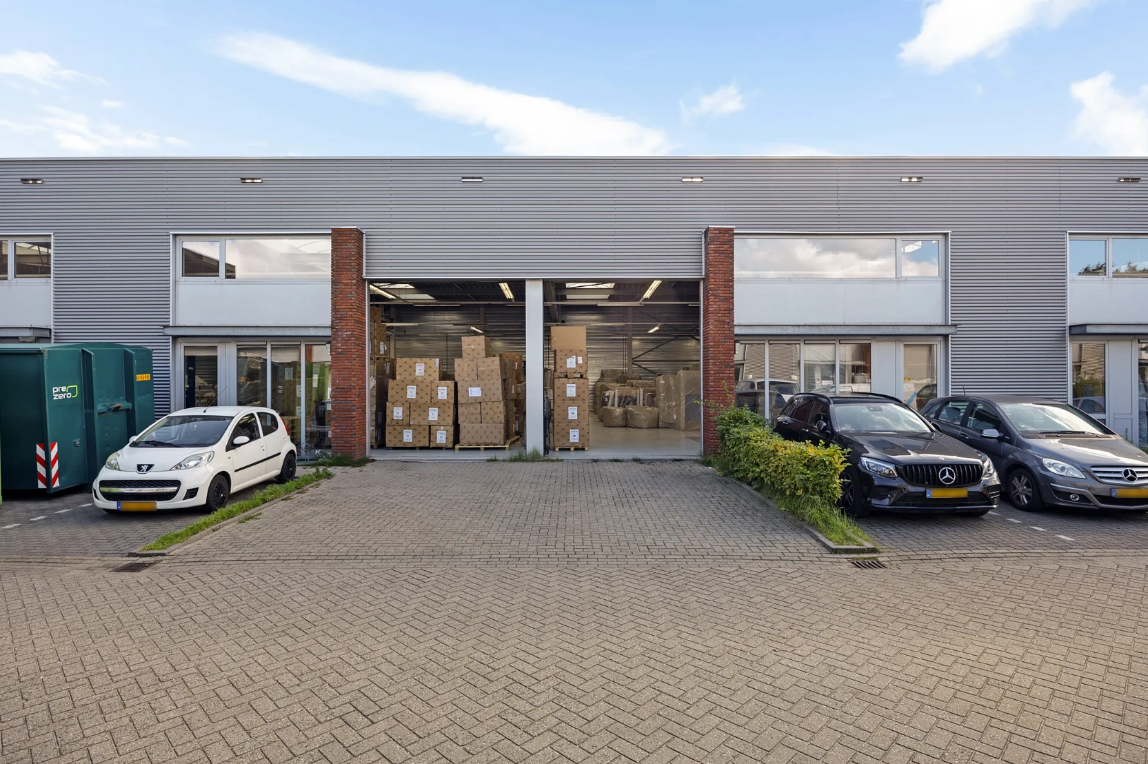 Bedrijfsgebouw aan de Schaafstraat met openstaande loodsdeuren en dozen op pallets binnen, omringd door geparkeerde auto's.