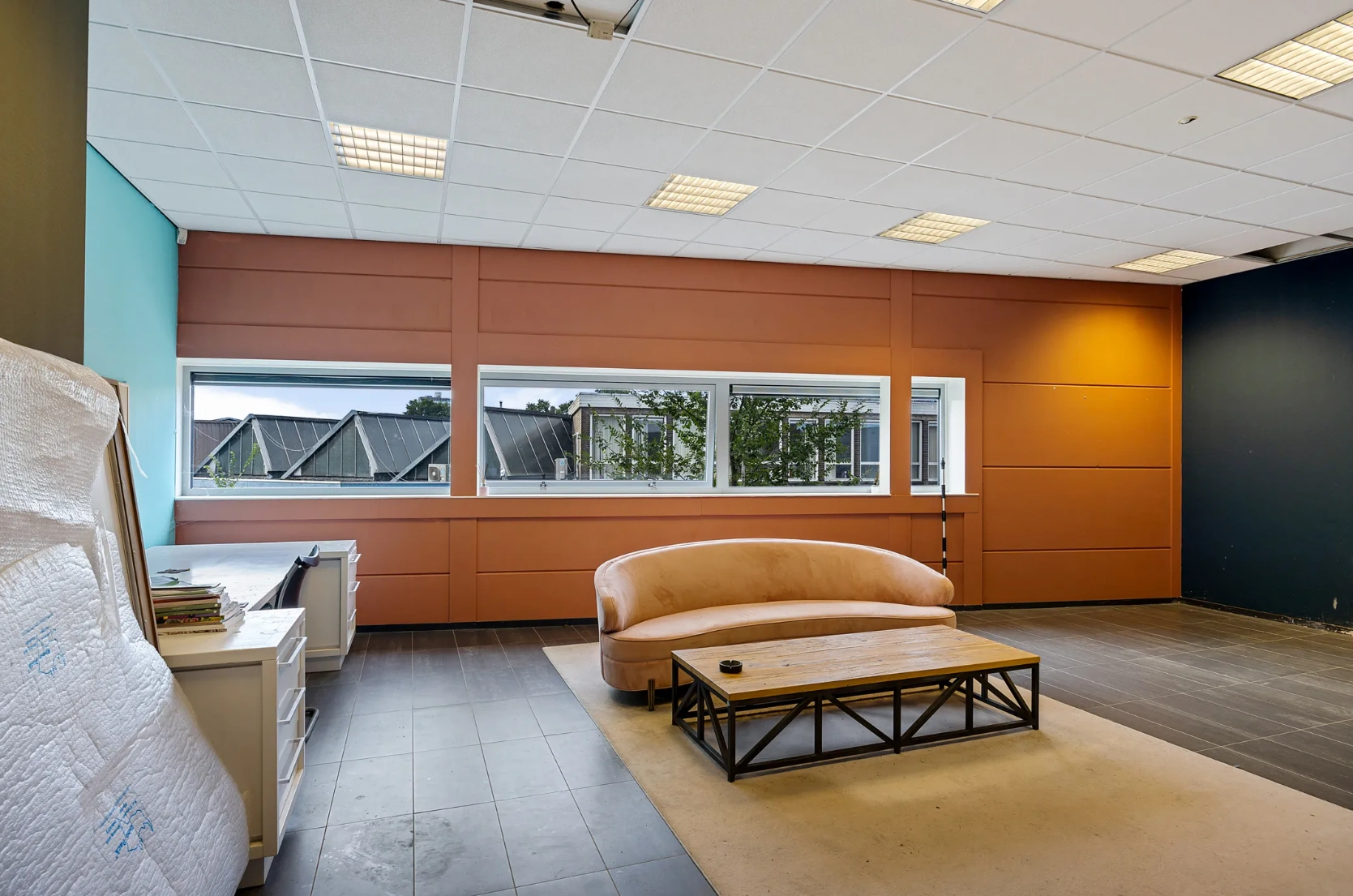 Kantoorruimte aan de Schaafstraat met grote ramen, een roze bank en houten salontafel op een beige vloerkleed.