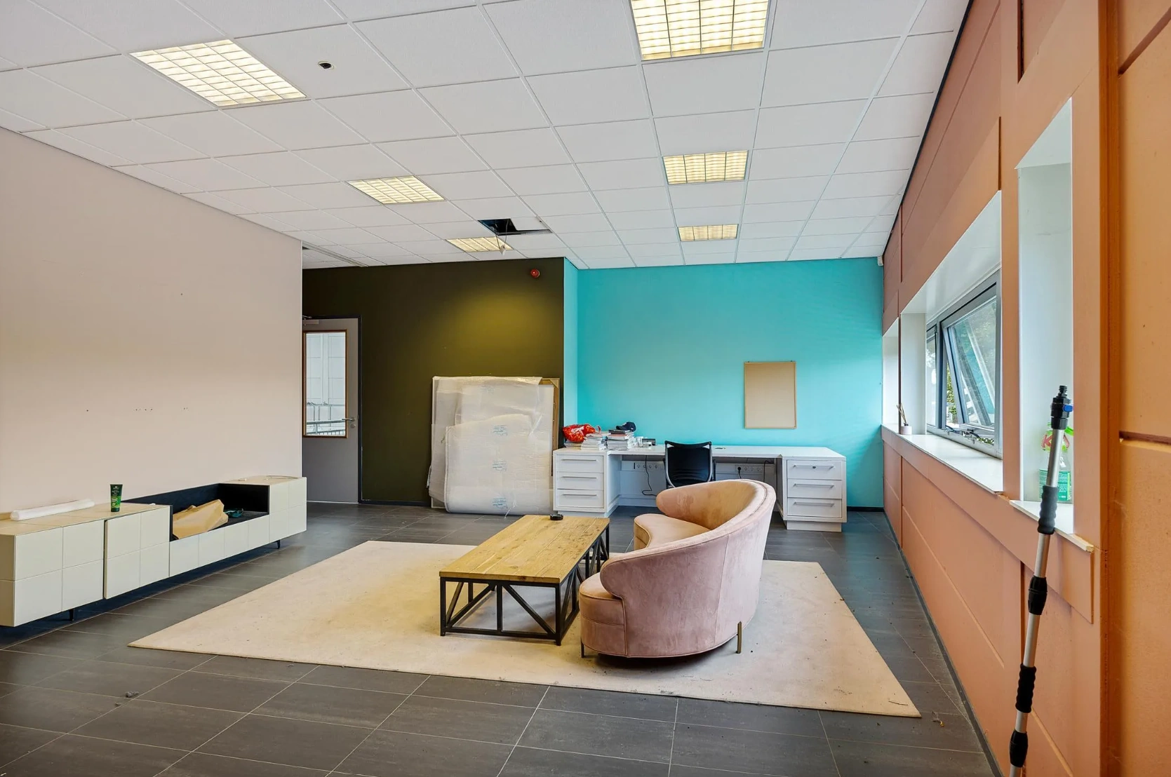 Kantoorruimte aan de Schaafstraat met een roze bank, houten salontafel en een werkplek tegen een turquoise muur.