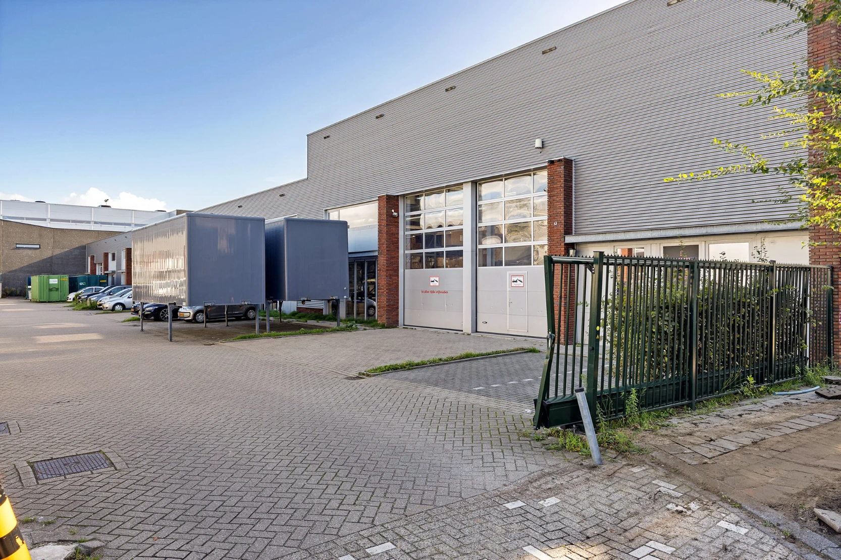 Vooraanzicht van een modern bedrijfsgebouw aan de Schaafstraat met laadperrons, geparkeerde voertuigen en een beschadigd hek.