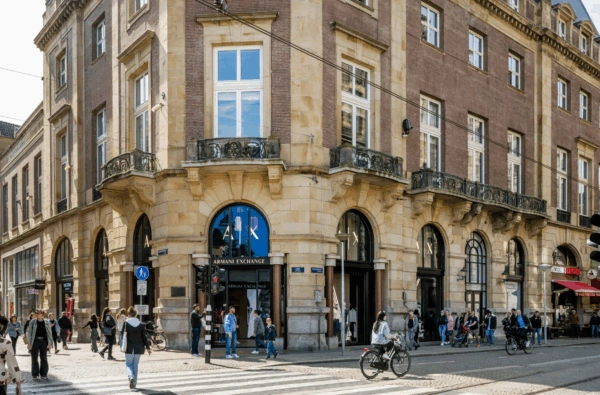 Drukke straat op de hoek van de Paleisstraat met winkels zoals Armani Exchange in een historisch gebouw.