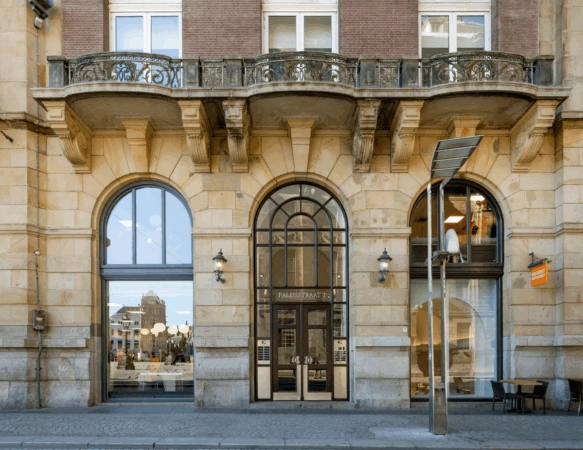 Voorgevel van een historisch gebouw aan de Paleisstraat 1 met grote boogramen, sierlijke balkons en een centrale ingang.
