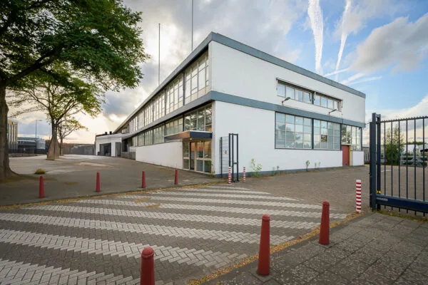 Wit modern kantoorpand aan de Linschotenstraat met grote ramen en een afgesloten parkeerterrein.