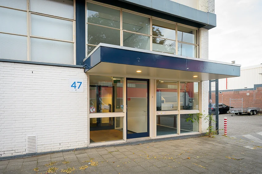 Ingang van een bedrijfsgebouw aan de Linschotenstraat 47 met glazen deuren en een blauw overstek.