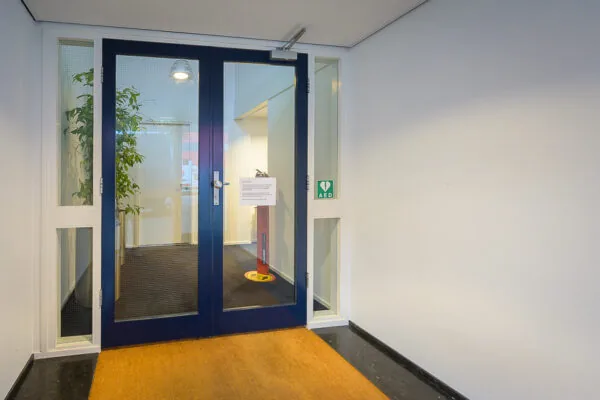 Dubbele blauwe glazen deur naar een kantoorruimte aan de Linschotenstraat met AED-aanduiding en gele mat.