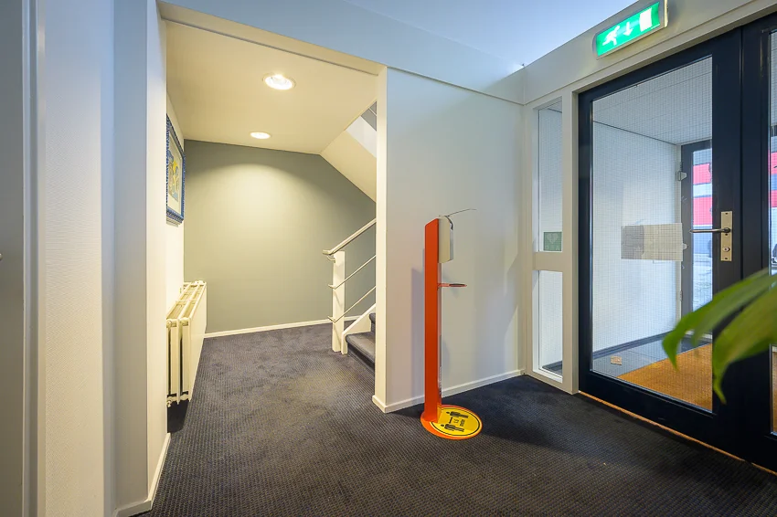 Entreehal van een appartementencomplex aan de Linschotenstraat met trapopgang, desinfectiezuil en nooduitgang.