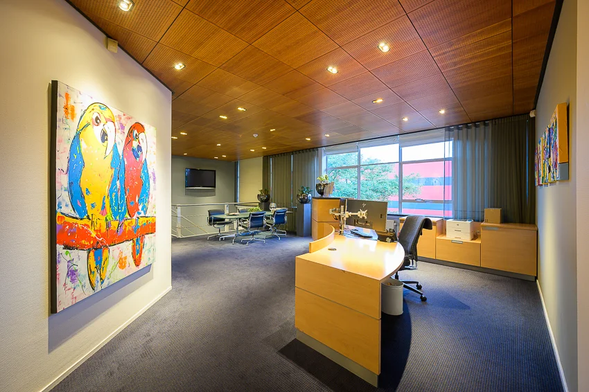 Modern kantoorinterieur aan de Linschotenstraat met houten meubels, kunst aan de muur en grote ramen.
