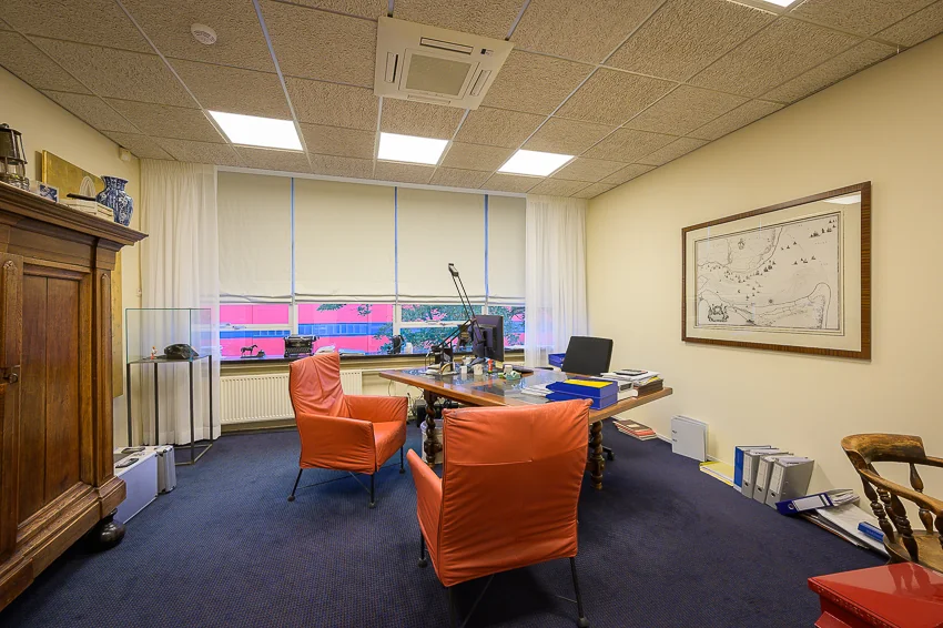 Kantoorruimte aan de Linschotenstraat met een houten bureau, oranje stoelen, archiefmappen en een grote wandkaart.