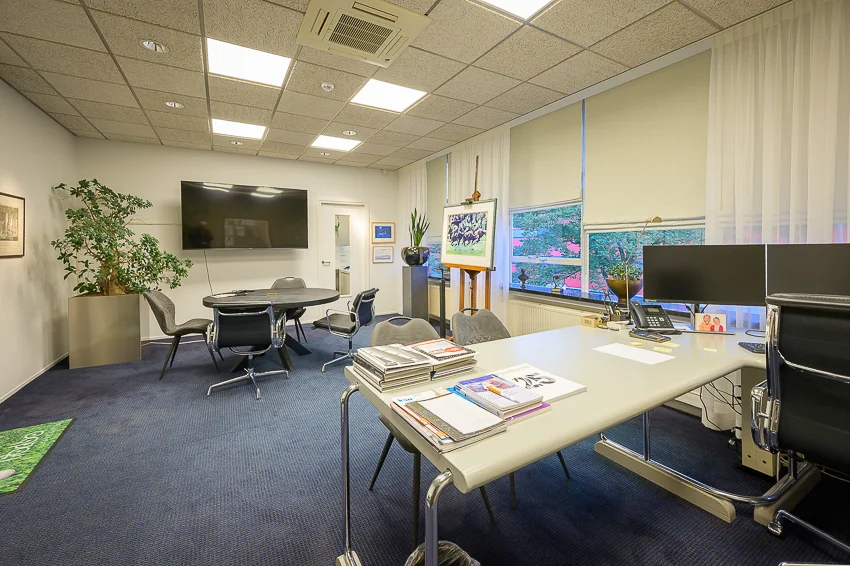 Moderne kantoorruimte aan de Linschotenstraat met een vergadertafel, bureau, grote tv en kunst aan de muur.