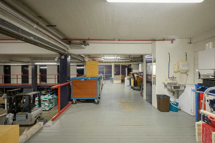 Binnenruimte van een industriële opslagruimte aan de Linschotenstraat met werkmateriaal, stellingen en een wasbak tegen de muur.