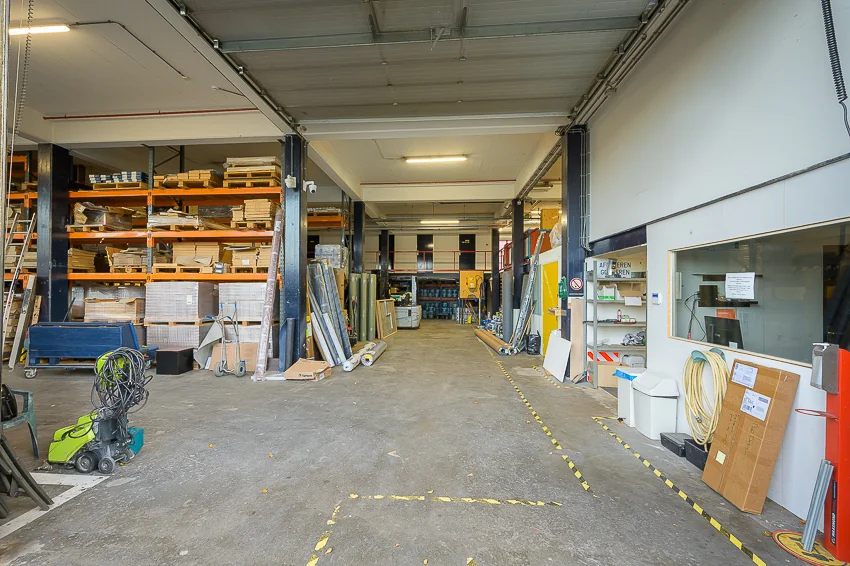 Interieur van een magazijn aan de Linschotenstraat met stellingen vol bouwmaterialen en een opslagruimte op de achtergrond.