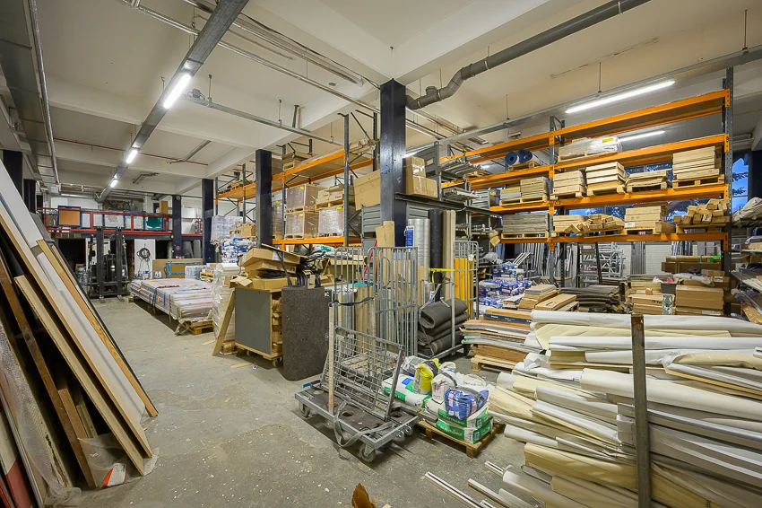 Magazijn aan de Linschotenstraat met stellingen vol bouwmaterialen, pallets en opgestapelde goederen.