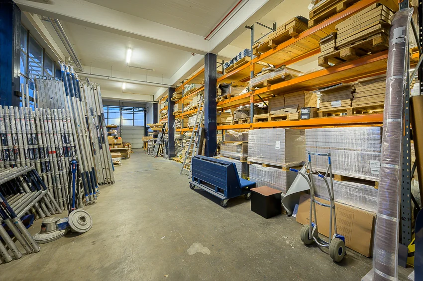 Magazijn aan de Linschotenstraat met hoge stellingkasten vol materialen en gereedschappen.