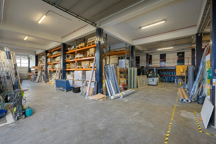 Magazijn aan de Linschotenstraat met stellingkasten vol bouwmaterialen en gereedschap.