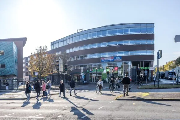 Drukke straat met voetgangers en fietsers bij een PLUS-supermarkt aan de Arnhemseweg.