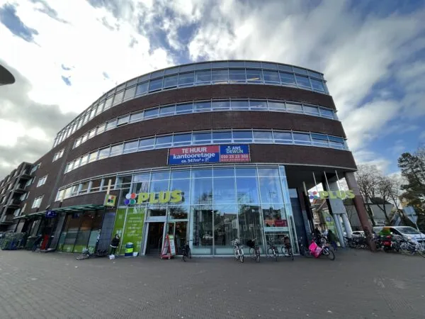 Vooraanzicht van een modern kantoorgebouw aan de Arnhemseweg met een PLUS supermarkt op de begane grond en een bord met kantoorruimte te huur.