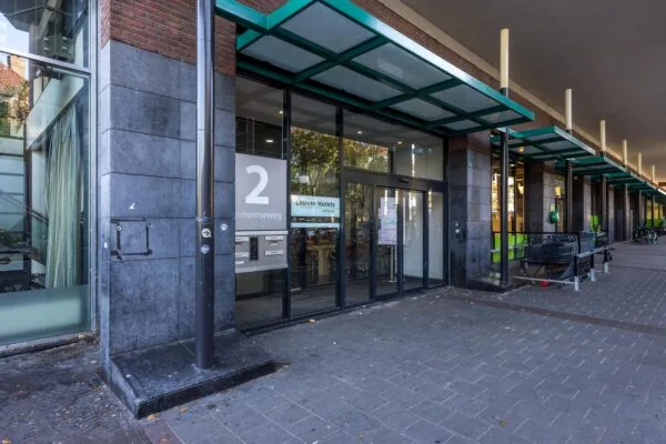 Ingang van gebouw aan de Arnhemseweg 2 met glazen deuren en overkapping, naast een rij winkelwagentjes.