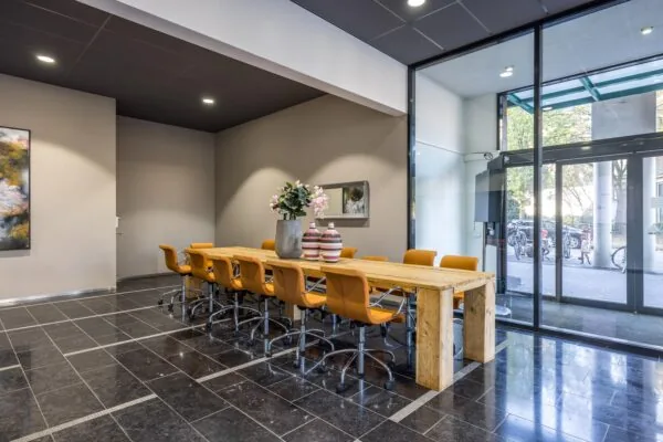 Moderne vergaderruimte aan de Arnhemseweg met een lange houten tafel, oranje bureaustoelen en grote glazen entree.