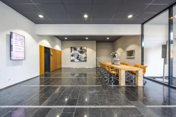 Moderne entree of wachtruimte aan de Arnhemseweg met lange houten vergadertafel, gele stoelen en kunst aan de muur.
