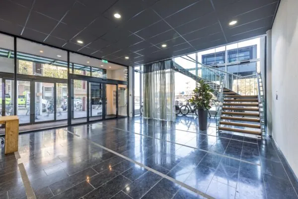 Moderne entreehal met glazen deuren, een open houten trap en uitzicht op de Arnhemseweg.